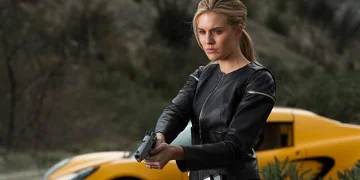 Lily Pointing A Gun Stood Infront Of A Yellow Sports Car